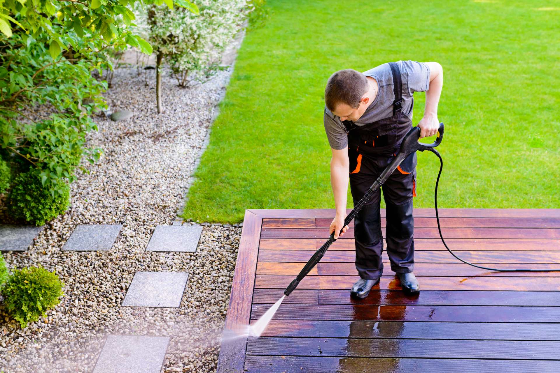 Persona limpiando un patio de madera con agua a presión